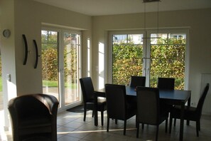 A dining area with a table and chairs, large windows, and a view of greenery outside. - Holiday home with 3 bedrooms (Boltenhagen)