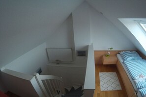 A bedroom with a sloped ceiling, a bed with striped bedding, a bedside table with a lamp, and a small window. - Holiday apartment with 2 bedrooms (Norderney)