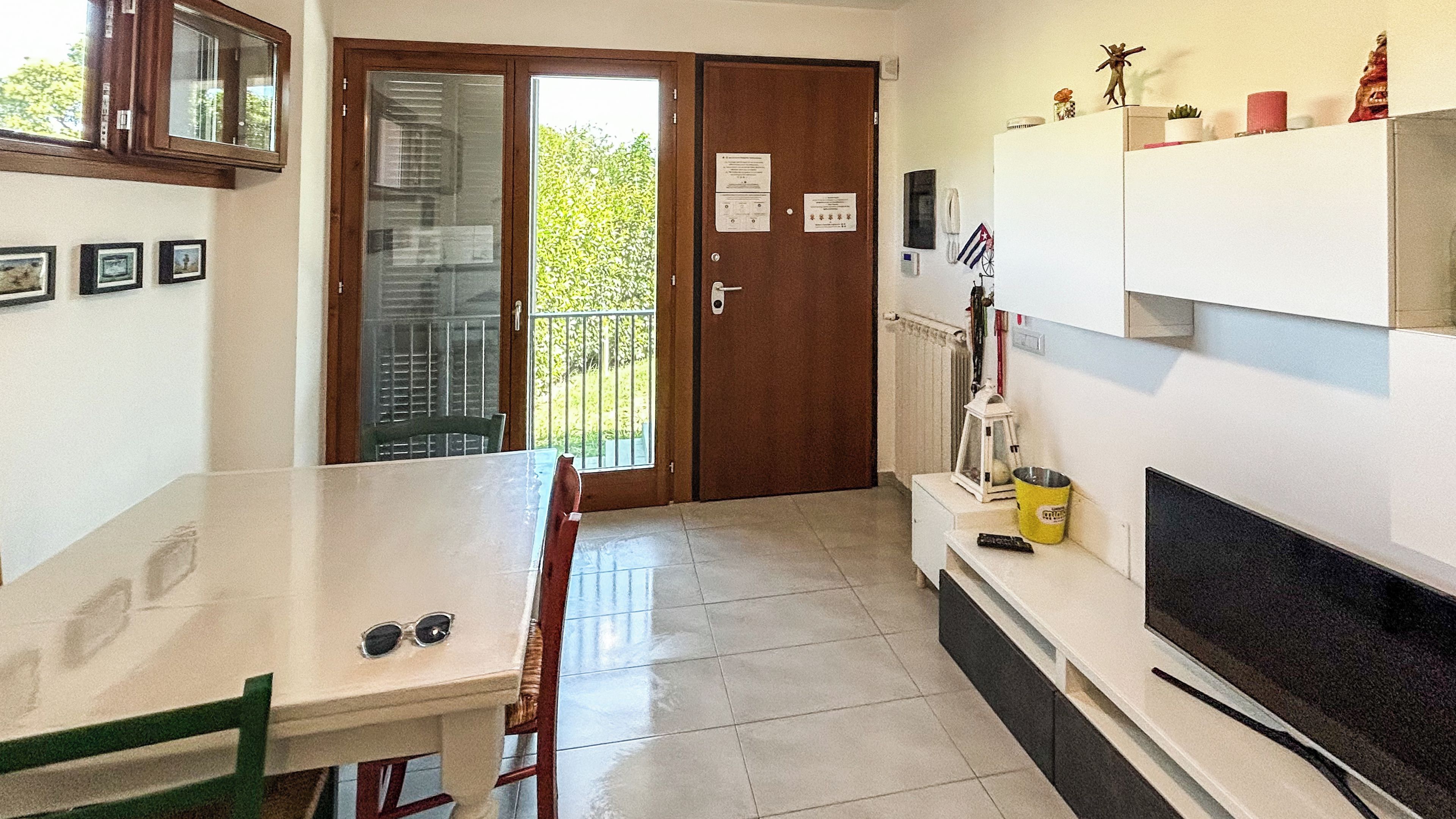 Une cuisine avec une table à manger, des chaises, un téléviseur et une porte donnant sur un balcon.