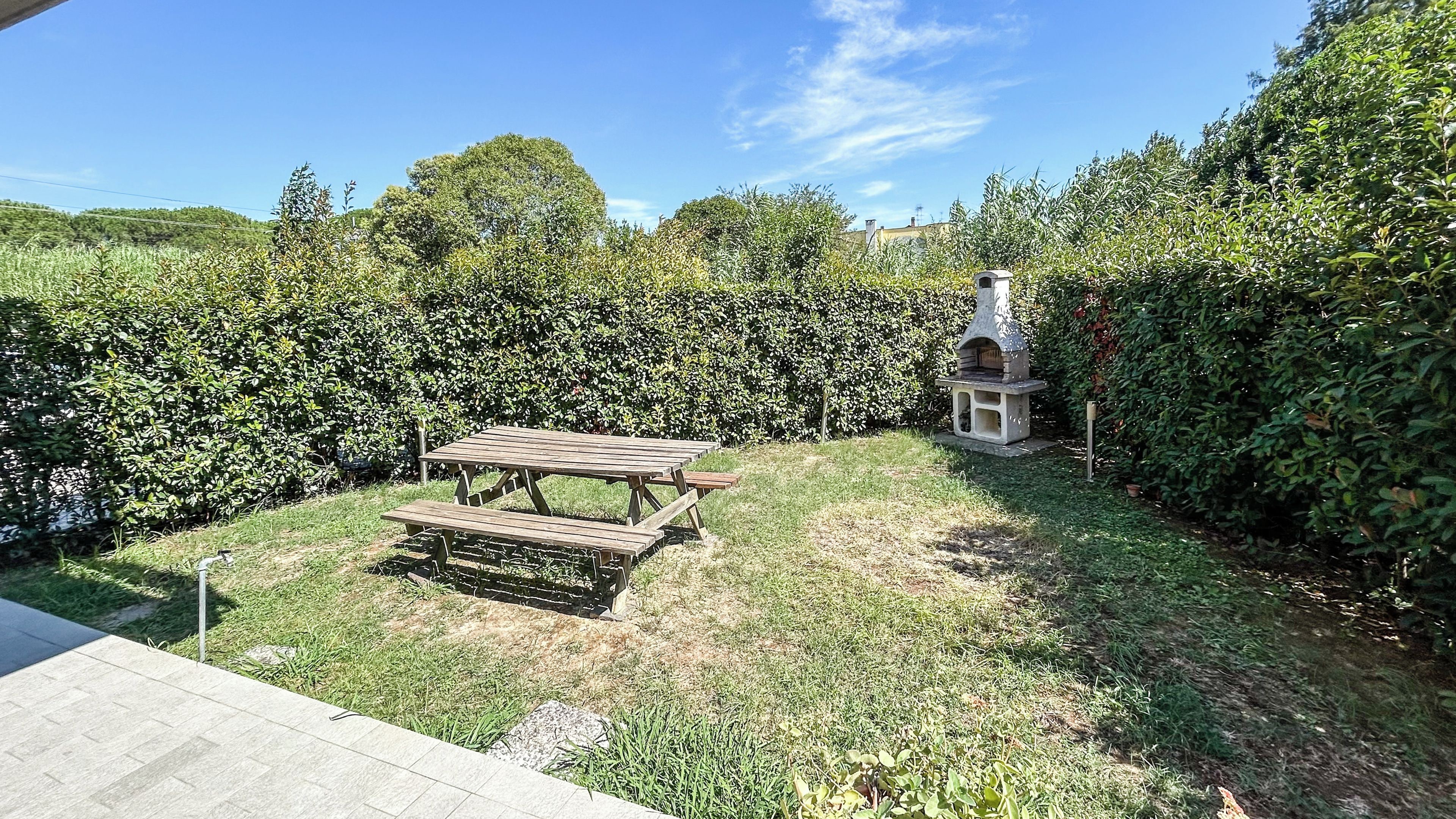 Un jardin avec une table de pique-nique en bois et un barbecue en pierre.