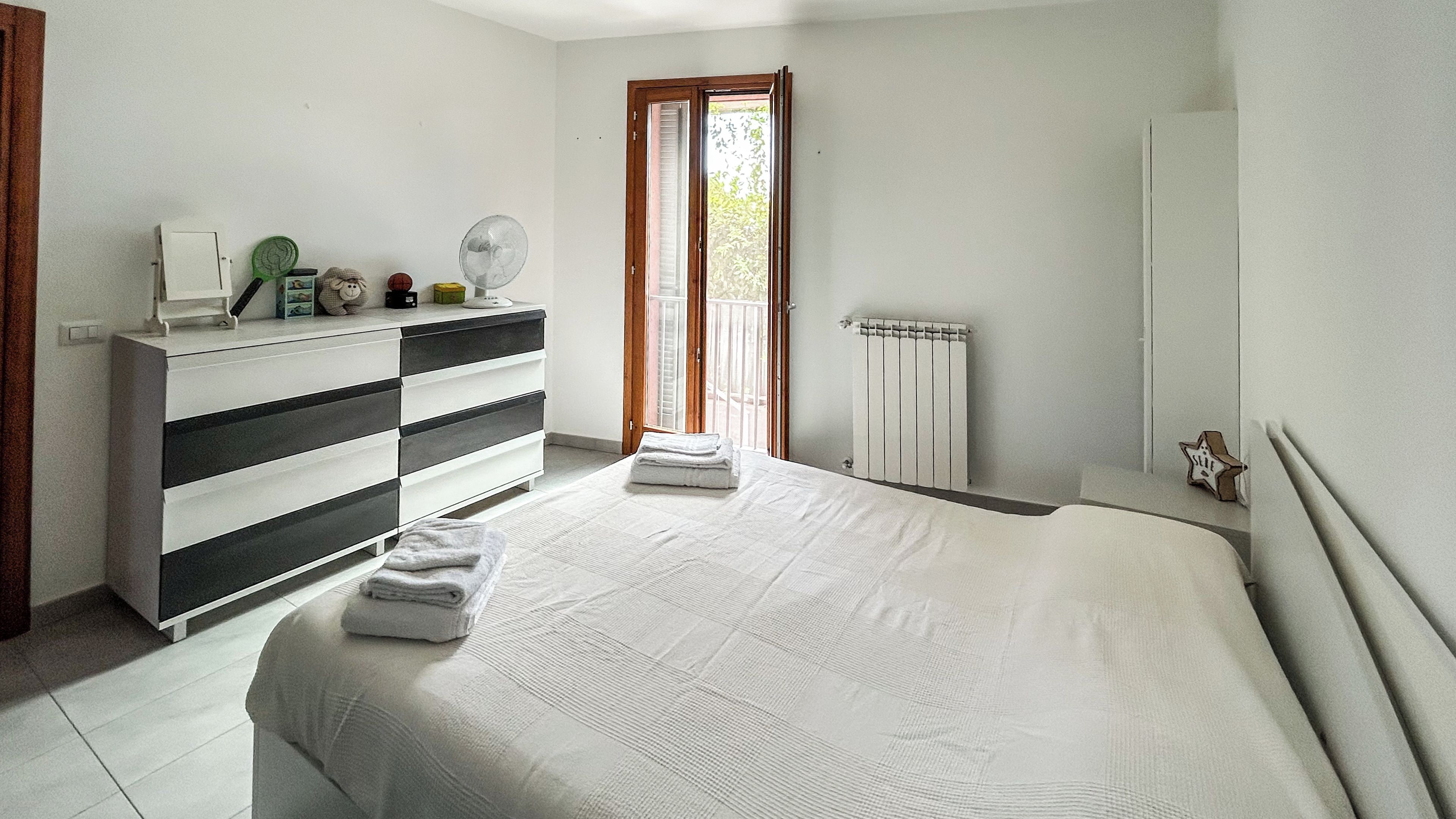 A bedroom with a bed, a dresser, a radiator, and a window with a view.