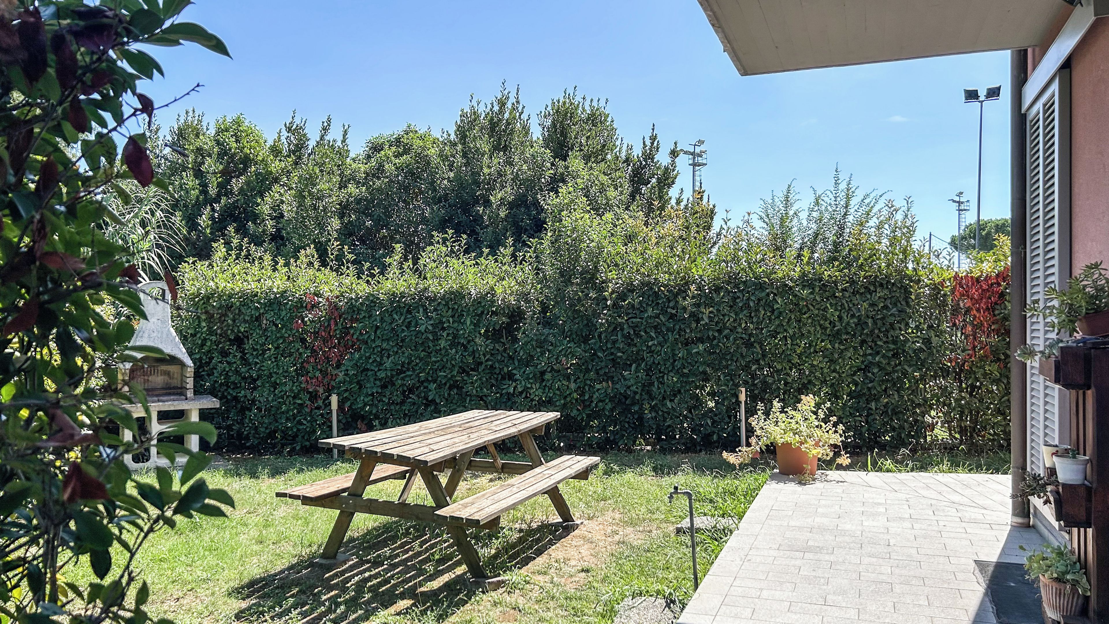 Een houten picknicktafel in een tuin, met een haag op de achtergrond.