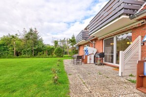 Ein Haus mit Terrasse, Grill und überdachter Sitzgelegenheit im Freien.