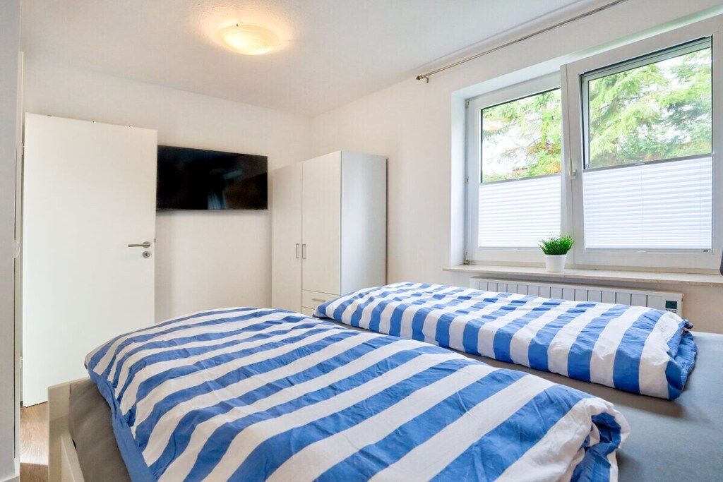 A bedroom with two beds, a white wardrobe, a television on the wall, and a window with blinds.