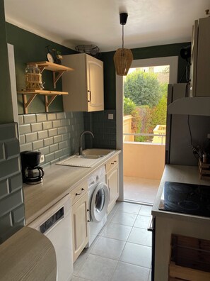 A compact kitchen with a built-in washing machine, a coffee maker, and a hanging light fixture. - 2 chambres dans appartement à Nice avec climatisation (Nice)