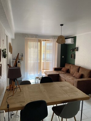 Ein modernes Wohnzimmer mit einem Holzes Esstisch, zwei Stühlen, einem Sofa und einer Hängelampe.