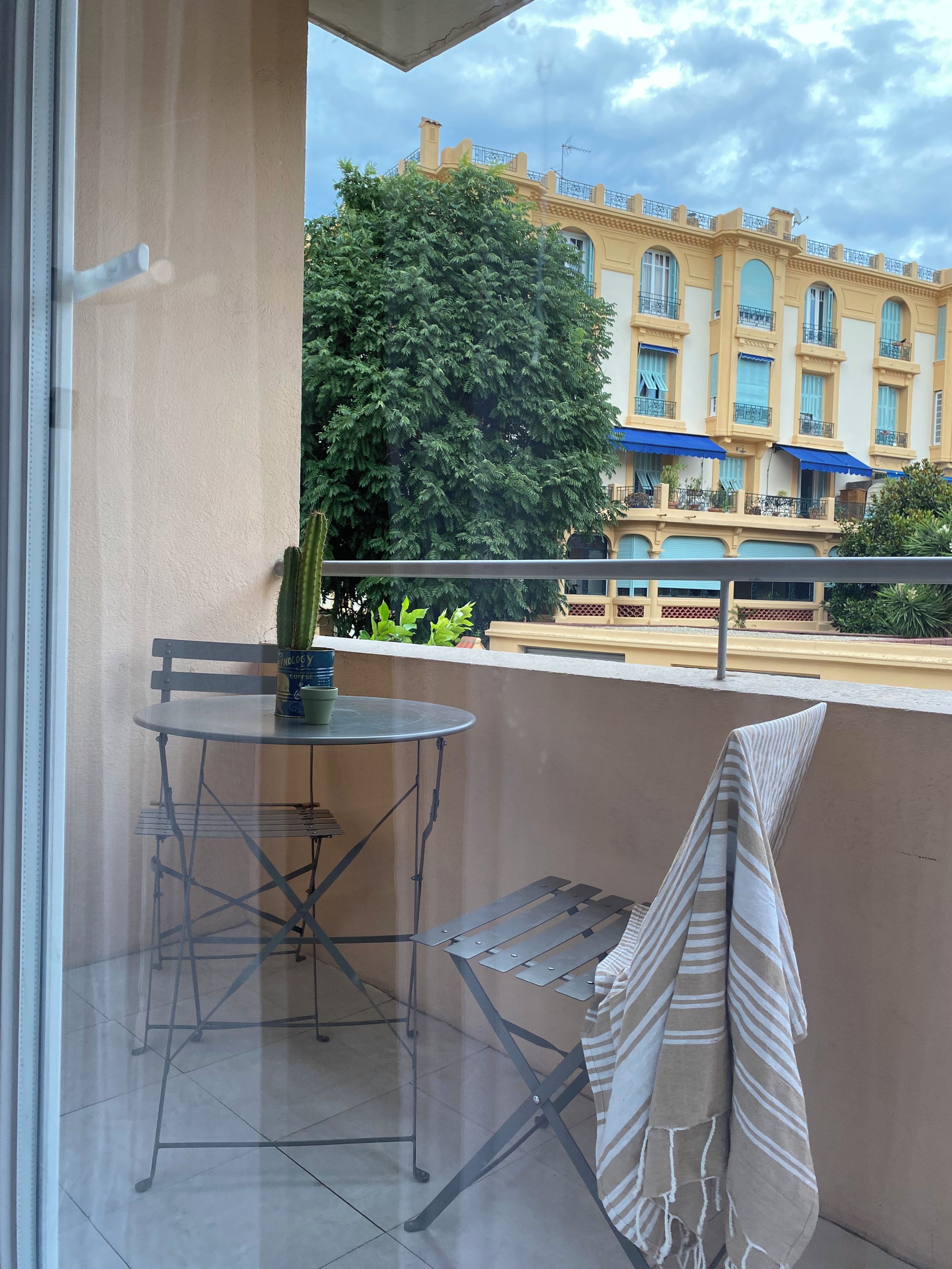 A balcony with a table and chairs, a striped towel, and a potted plant.