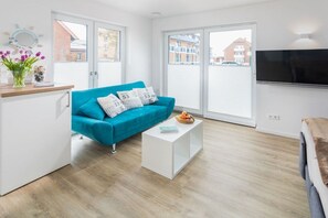 Ein modernes Wohnzimmer mit einem türkisfarbenen Sofa, einem weißen Couchtisch und einem wandmontierten Flachbildfernseher.