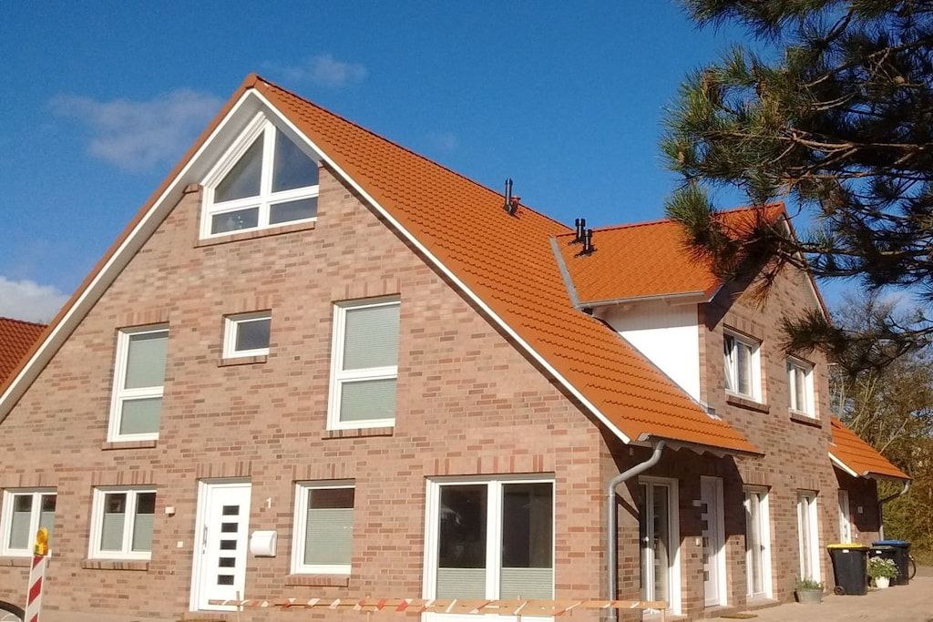 Una casa de ladrillo de dos pisos con techo de tejas rojas, múltiples ventanas y una chimenea visible.