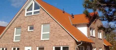 Una casa de ladrillo de dos pisos con techo de tejas rojas, múltiples ventanas y una chimenea visible.