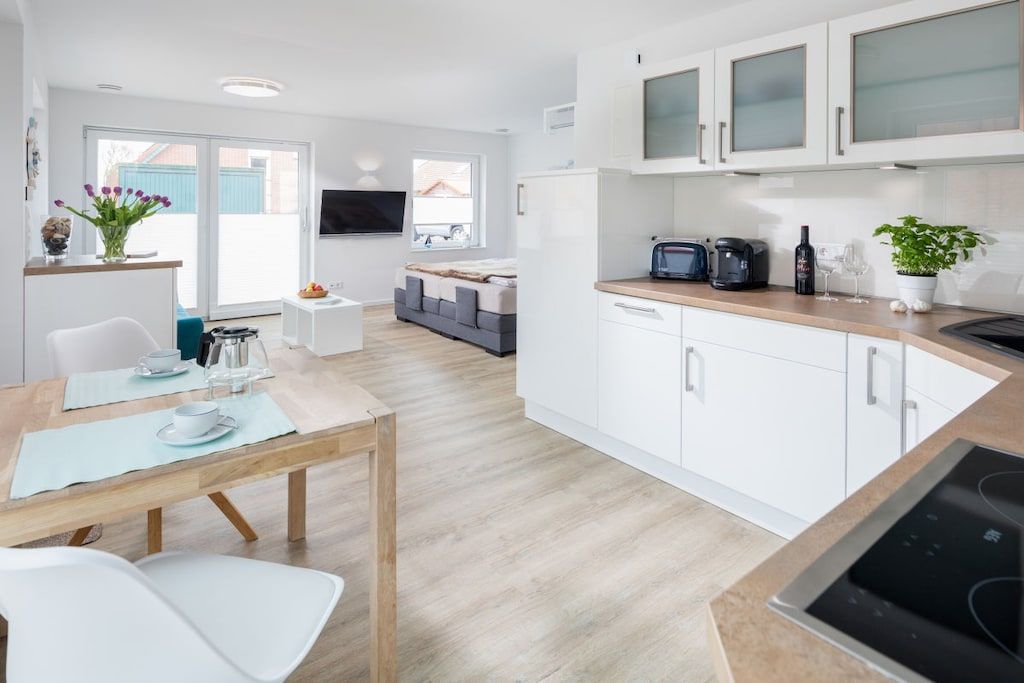 Een moderne keuken met witte kasten, een eethoek met tafel en stoelen, een bank en een aan de muur bevestigde televisie.