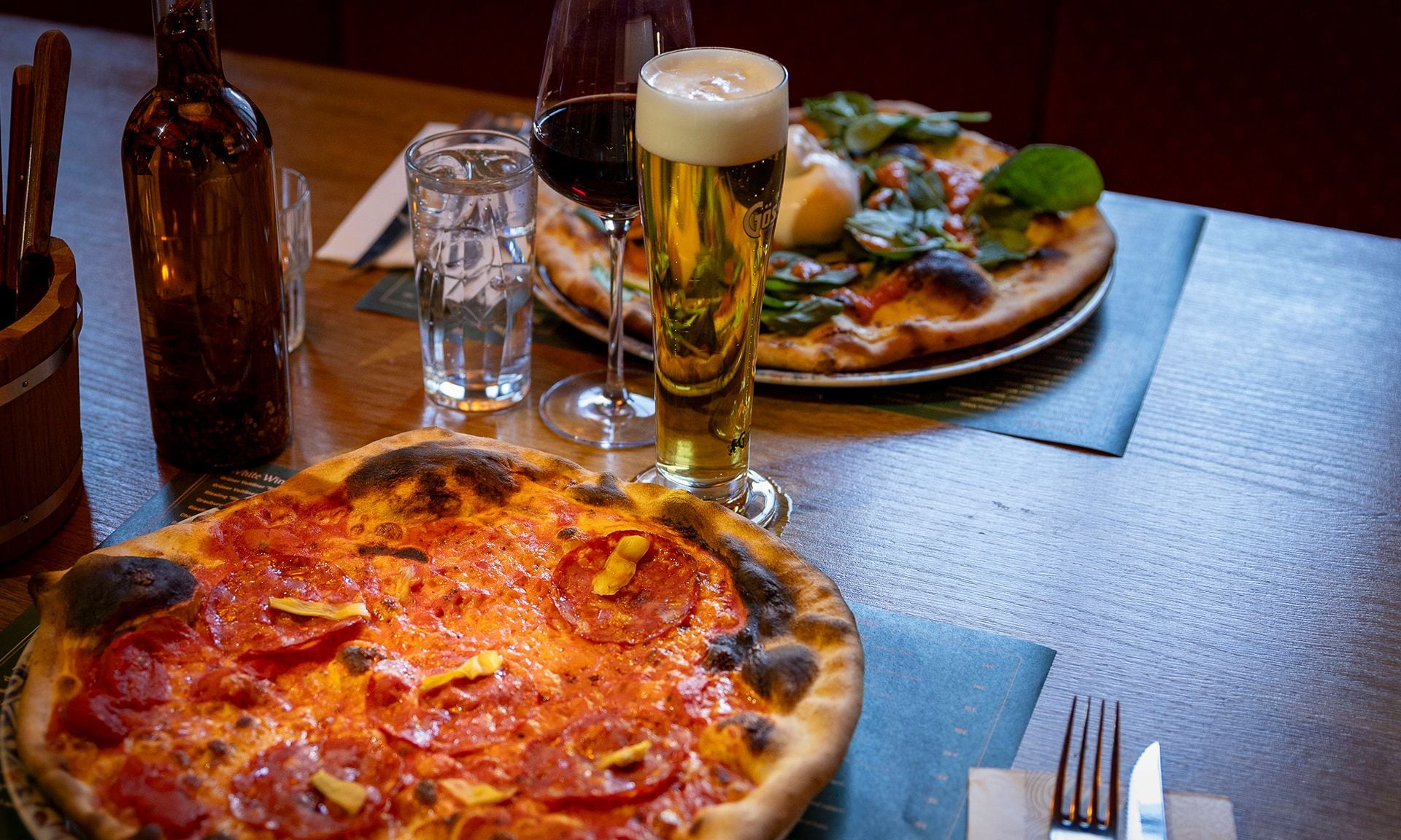Pizza con pepperoni y un vaso de cerveza sobre una mesa de madera.