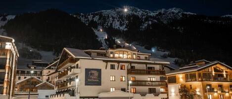 A multi-story hotel with a ski resort backdrop, featuring balconies and a prominent sign.