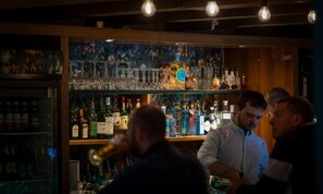 Eine Bar mit Flaschenregalen und Gläsern, ein Barkeeper und Gäste.