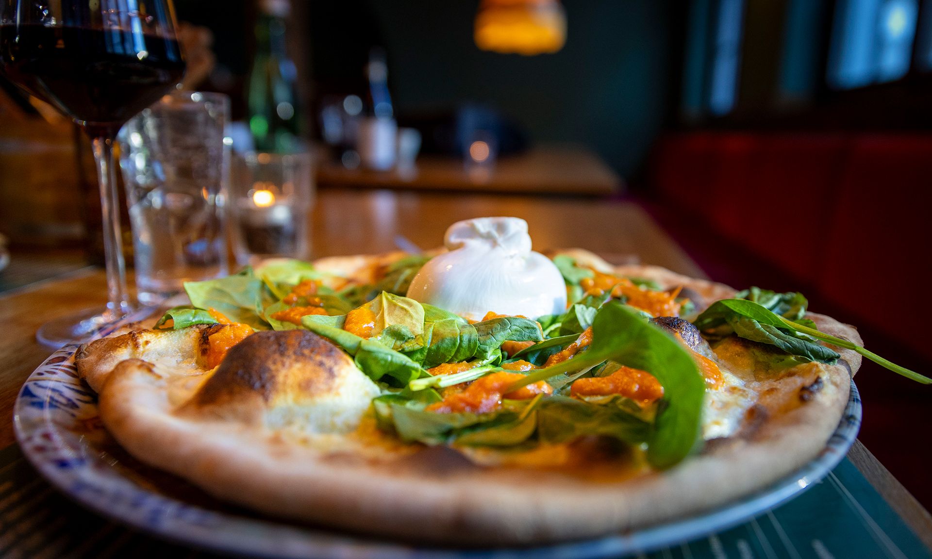 A pizza with a dollop of cream on a plate, accompanied by a glass of red wine and a bottle in the background.