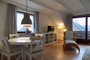 A cozy living room with a round table, white chairs, a television, and a comfortable chair. - House Gröde Holiday Apartment 4 (Wenningstedt)