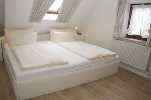 A bedroom with a large bed, a bedside table, a window with curtains, and a radiator. - House Gröde Holiday Apartment 4 (Wenningstedt)