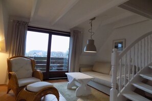 A living room with a sofa, a chair, a small table, and a staircase. - House Gröde Holiday Apartment 4 (Wenningstedt)