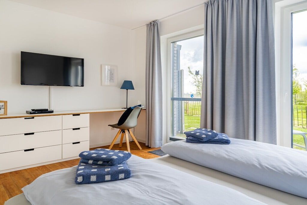 Une chambre d’hôtel comprenant un lit, un bureau avec un téléviseur à écran plat, une chaise et une fenêtre avec des rideaux.