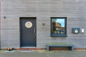 Eine Gebäudefassade mit einer dunklen Tür, einem Fenster und einer Bank.