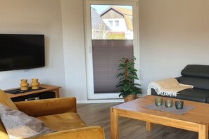 Un salon comprenant un canapé, une table basse, un téléviseur et une porte-fenêtre coulissante donnant sur un espace extérieur.