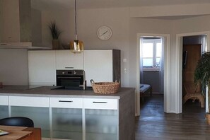 A modern kitchen with a central island, a dining area with a table, and a living space with a sofa and a plant. - Holiday apartment with 2 bedrooms (Hohwacht)