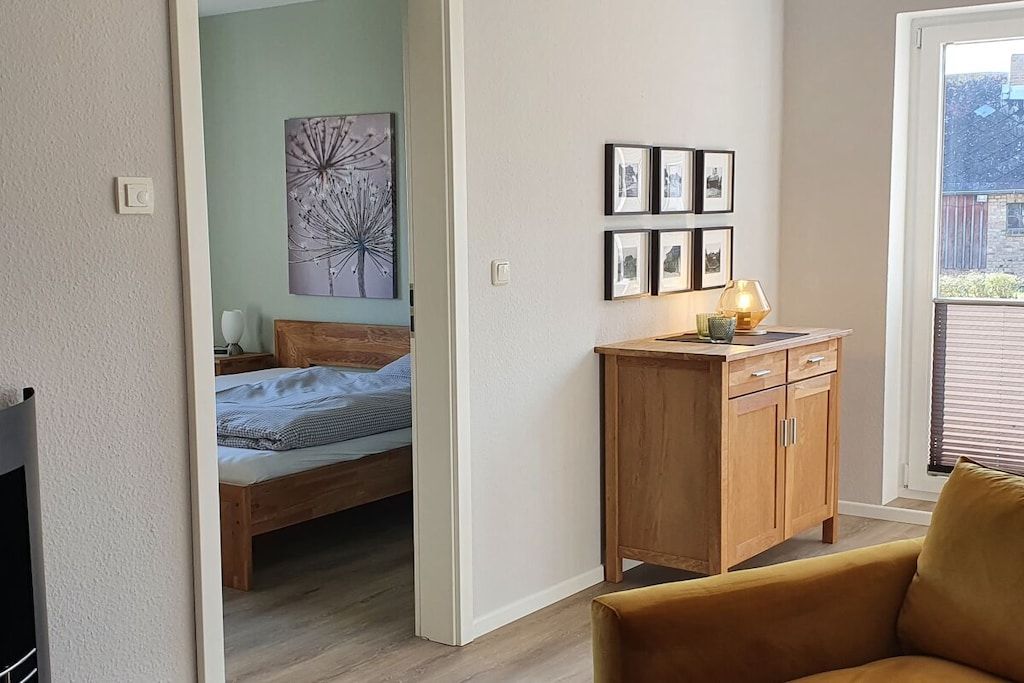 Een slaapkamer met een bed, een houten nachtkastje, een nachttafel met een lamp en een wand met ingekaderde foto's.