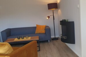 A modern living room with a sofa, a coffee table, a floor lamp, and a wall-mounted shelf. - Holiday apartment with 2 bedrooms (Hohwacht)
