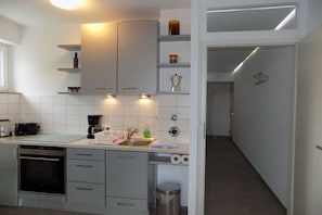 A modern kitchen with white cabinets, a built-in oven, and a coffee maker. - Theodor-Heuss-Str. Holiday Apartment 11 (Westerland)