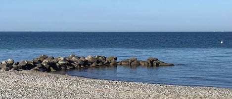 Una playa de guijarros con un rompeolas rocoso que se adentra en el mar.
