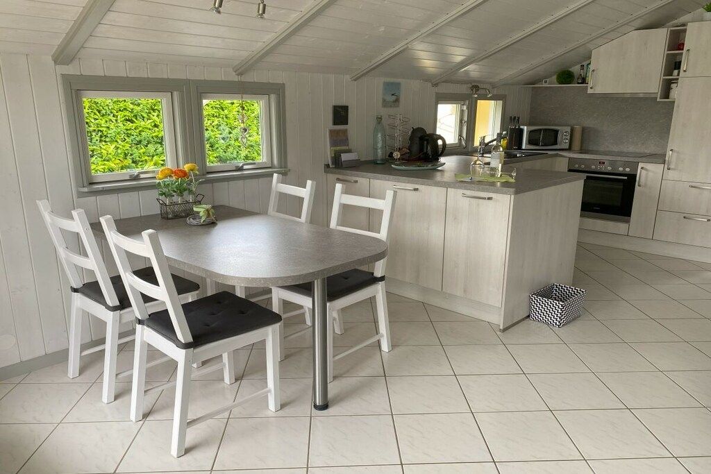 A kitchen with a central island, white cabinetry, and a dining area with chairs.