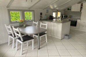 Een keuken met een centraal eiland, witte kastjes en een eethoek met stoelen.