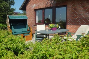 Eine Terrasse mit Tisch und Stühlen, einer Schaukel und einem Backsteinhäuschen im Hintergrund.