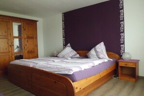 Un letto singolo con struttura in legno e materasso viola, un comodino in legno con una lampada e un armadio con ante in vetro.
