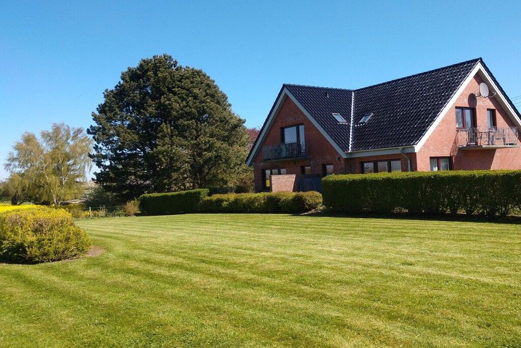 Une maison à deux étages avec un toit en pente, un balcon au deuxième étage et une pelouse bien entretenue.