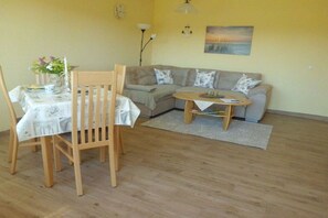 A living room with a wooden dining table, a sofa, and a small coffee table. - Holiday apartment with 1 bedroom (Hasselberg)