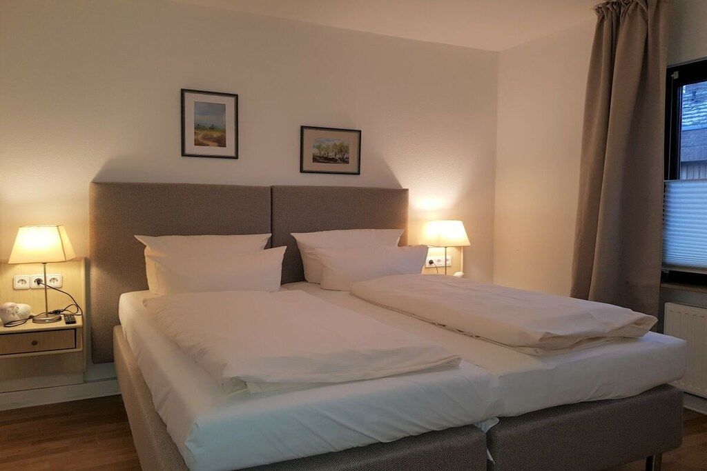 A double bed with white linens, two bedside tables with lamps, and two framed pictures on the wall.
