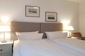 A hotel room with a bed, two bedside lamps, a nightstand, and two framed pictures on the wall. - Ground floor holiday apartment Zur Eiche 19 (Tinnum \/ Sylt)