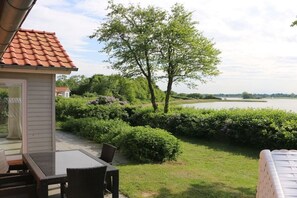 Une terrasse avec une table et des chaises, une vue sur un lac et un bâtiment avec un toit rouge.
