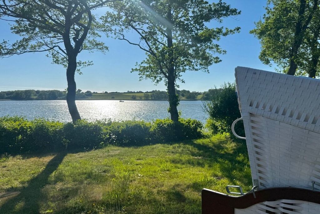 Ein Stuhl mit Blick auf einen See, Bäume und einen klaren Himmel.