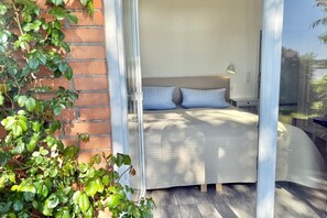 A bedroom with a bed, a nightstand, a lamp, and a view through a glass door. - Marina Hülsen - The Willow River House (Kosel)
