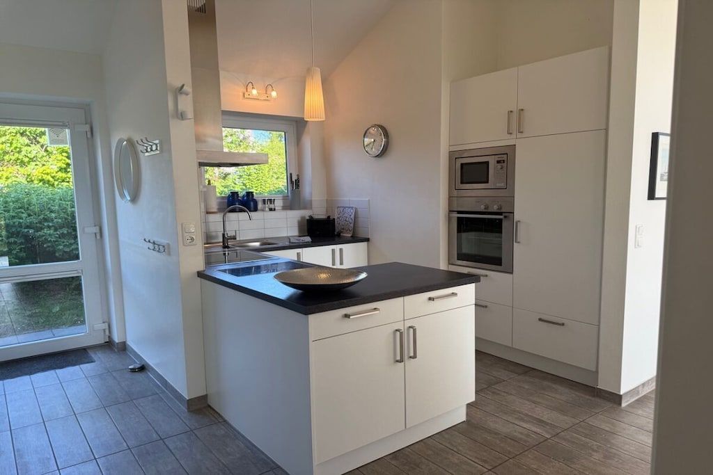 A modern kitchen with white cabinetry, a black countertop, and stainless steel appliances.