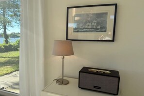 A framed picture on the wall, a lamp, and a radio on a table. - Marina Hülsen - The Willow River House (Kosel)