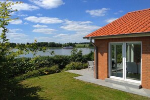 A house with a red-tiled roof, a glass door entrance, and a view of a lake with boats. - Marina Hülsen - The Reed Bank House (Kosel)