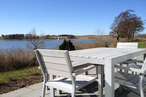 Un espace extérieur aménagé avec des meubles blancs, comprenant une table et des chaises, et offrant une vue sur une étendue d’eau.