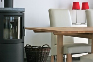A modern interior with a wood-burning stove, a wicker basket, and two chairs with red lamps. - Marina Hülsen - The Reed Bank House (Kosel)