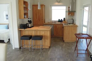 A compact kitchen with wooden cabinets, a central island with stools, a small dining table, and a window providing natural light. - Marina Hülsen - The Reed Bank House (Kosel)