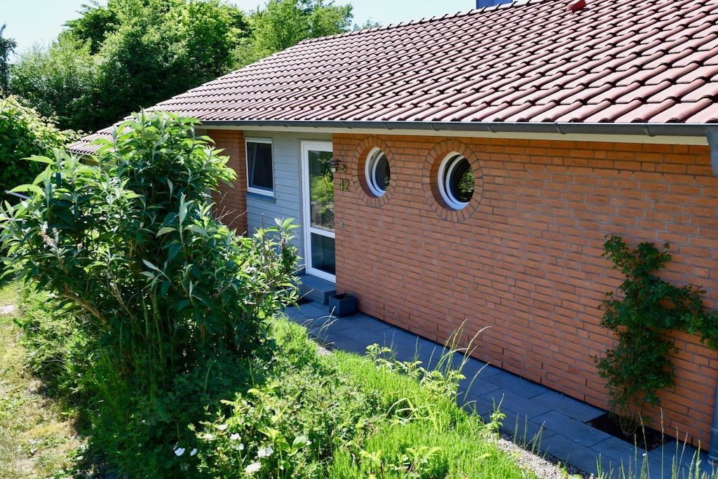 A single-story brick house with a red-tiled roof, two circular windows, and a door.