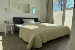 Une chambre à coucher avec un lit, une table de chevet, une petite table avec une plante, une fenêtre avec des rideaux et un miroir sur le mur.