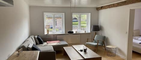 A modern living room with a sofa, a coffee table, and a chair. There are two windows with a view of the outside.